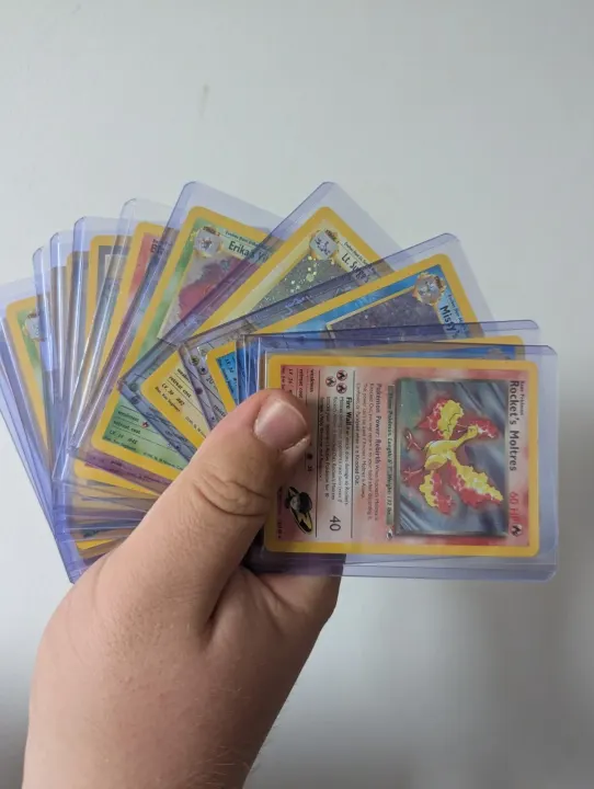 A hand holding a fan of around fifteen sleeved Gym-era holographic cards, a Rocket's Moltres on top.